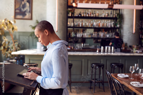 Female Owner Of Restaurant Bar Standing At Counter Using Digital Tablet photo
