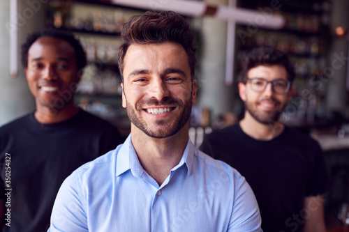 Portrait Of Male Owner Of Restaurant Bar With Team Of Waiting Staff Standing By Counter