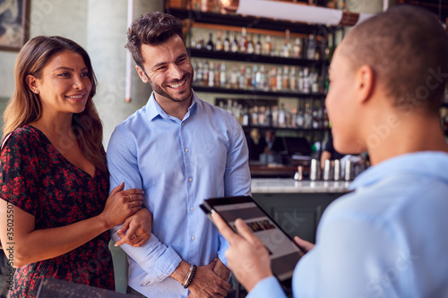 Couple Being Greeted By Maitre D Using Digital Tablet As They Arrive At Restaurant © Monkey Business