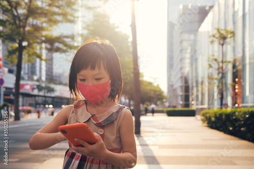 Asian child wearing mask and using cell phone in city