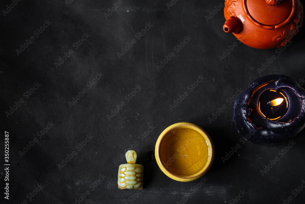 A cup of Chinese tea, teapot, candle, nephritis figure on a black background