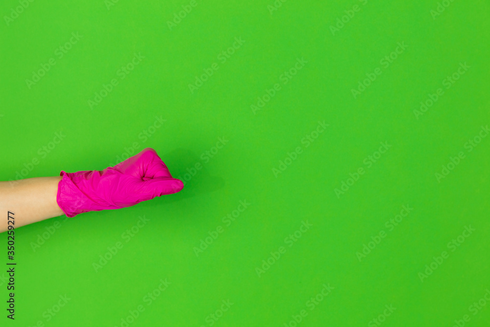 Hand in pink protective rubber glove shows fist bumb isolated on green studio background with copyspace. Gesturing, holding, presenting things. Negative space for your advertising. Showing, pointing. Hand in pink protective rubber glove shows fist bumb isolated on green studio background with copyspace. Gesturing, holding, presenting things. Negative space for your advertising. Showing, pointing.