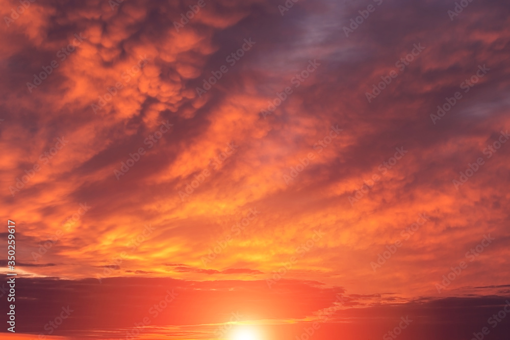 Epic dramatic sunset, sunrise red orange sky with mammatus clouds, sun and sunlight