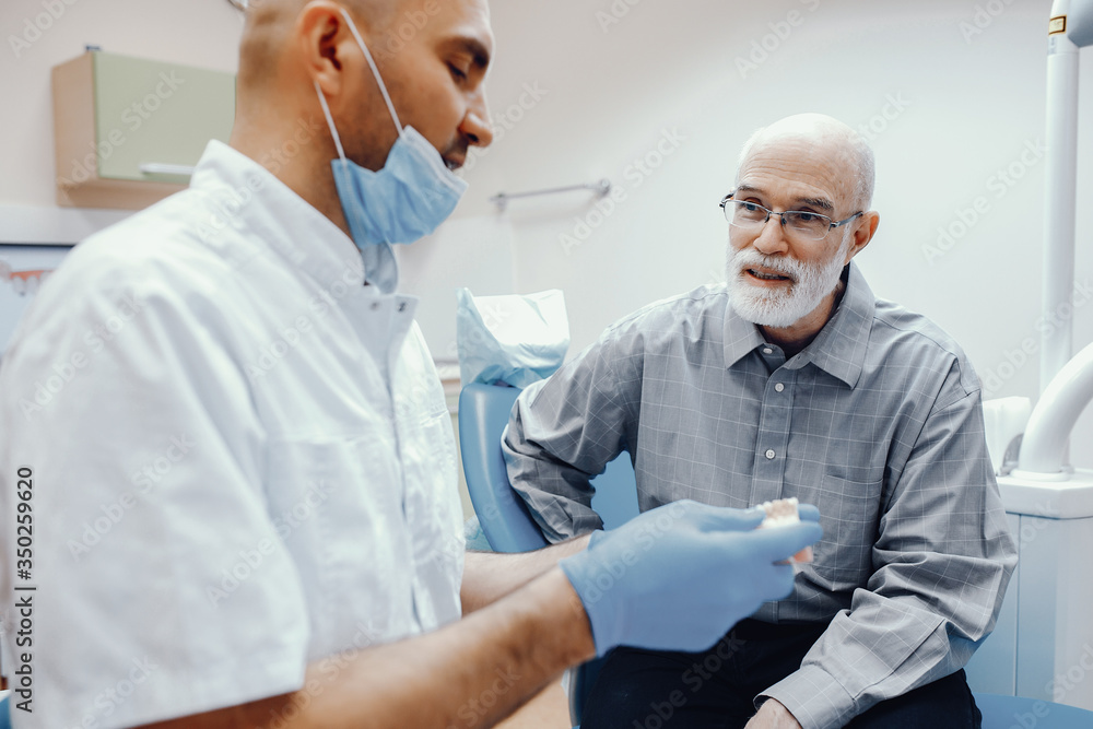 Handsome old man talking to the dendist. Two men in the dentist's office. The doctor shows the patient dentures Handsome old man talking to the dendist. Two men in the dentist's office. The doctor shows the patient dentures
