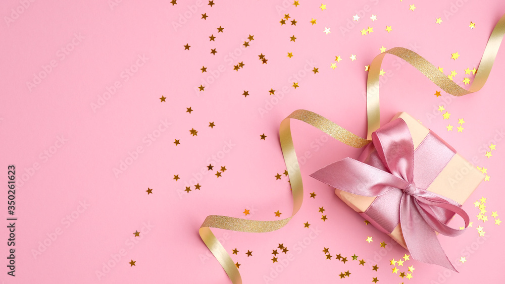 Fashion gift box with pink ribbon bow, golden streamer and confetti star on pink background top view. Flat lay composition for birthday, christmas or wedding. Fashion gift box with pink ribbon bow, golden streamer and confetti star on pink background top view. Flat lay composition for birthday, christmas or wedding.