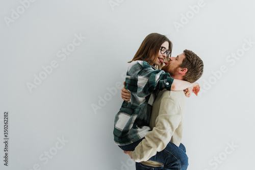 A man holds a woman in his arms and smiles. Man and women hug and kiss on a white background.