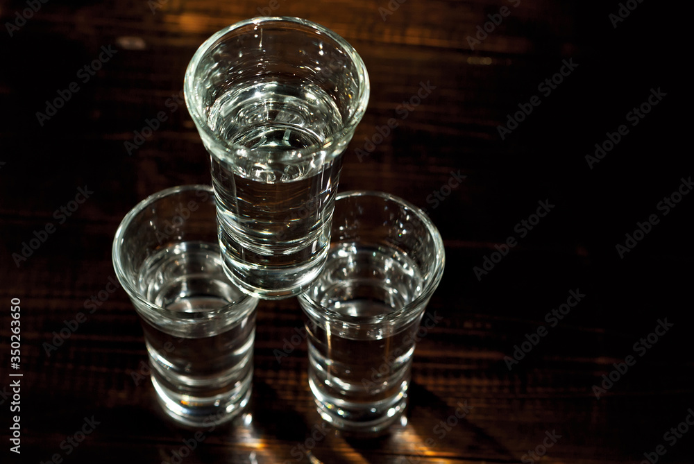 Glasses with alcohol close up. Vodka on a brown wooden background. Glass table from worn shabby boards. The glasses are stacked in a pyramid.