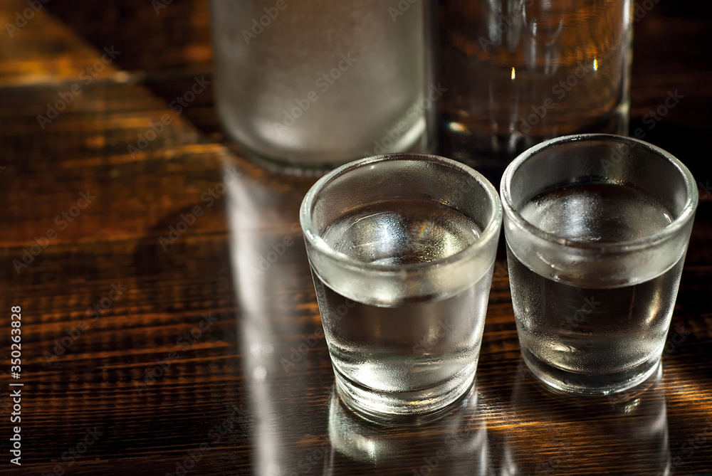 Frozen glasses with alcohol near the bottle. Drinks on a dark brown table. Transparent utensils on a black background. Old shabby boards under glass. Frozen glasses with alcohol near the bottle. Drinks on a dark brown table. Transparent utensils on a black background. Old shabby boards under glass.