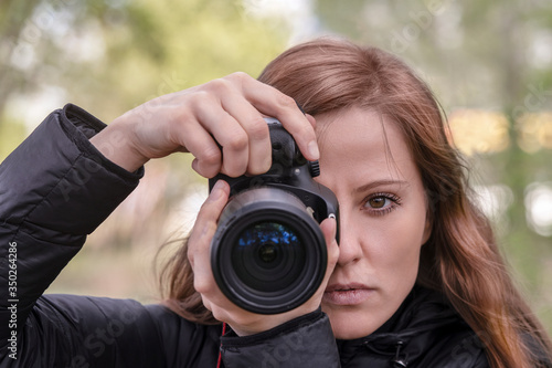 A beautiful woman photographer holds a camera in her hands and looks at the lens and the viewer. portrait, face close-up