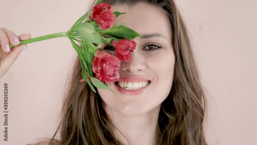 Portrait of young beautiful girl with long brown hair smiles and playfully closes her eyes with red flowers Portrait of young beautiful girl with long brown hair smiles and playfully closes her eyes with red flowers