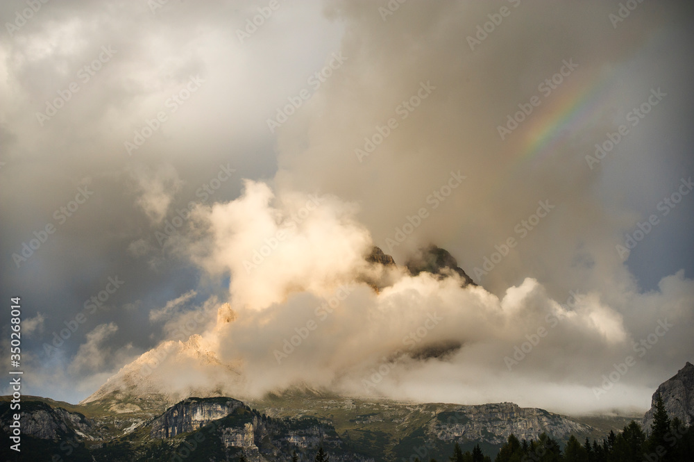 Arcobaleno al tramonto tra le nuvole e le montagne delle Dolomiti di Belluno