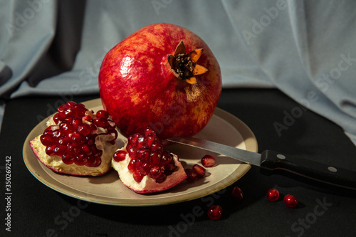 The whole pomegranate and its slices lie on a plate on black and gray and background.