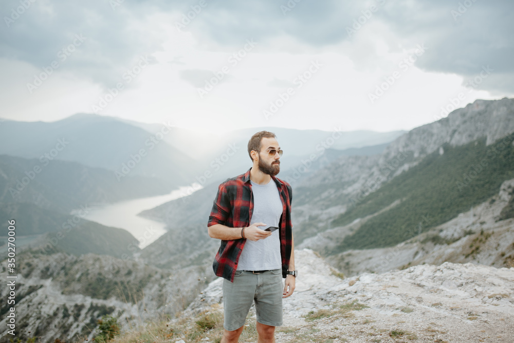 Portrait of a young man at a mountain top holding a mobile phone. Friends having a casual picnic in the mountains.