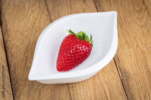 Fresh strawberry fruit in white dish on wooden background.