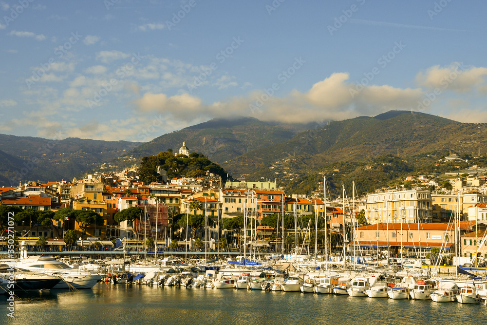 Scenic view of the harbor of Sanremo in the Riviera of Flowers with moored yachts and sailboats and the coastal city in the background in a sunny day, Imperia, Liguria, Italy