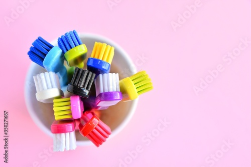 Colorful new plastic toothbrushes in white mug on pink neutral background  top view   selective focus  copy space. Trendy health care concept 