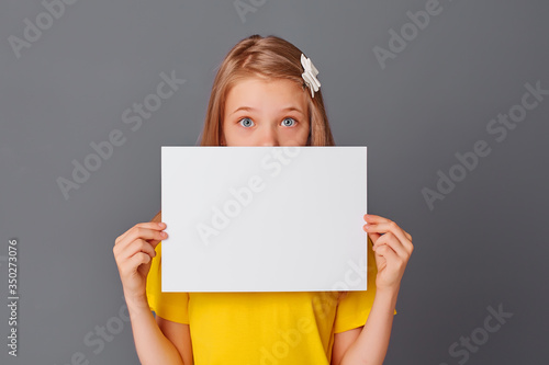 teen girl in yellow t-shirt holding empty white paper close-up, space for text, copy space
