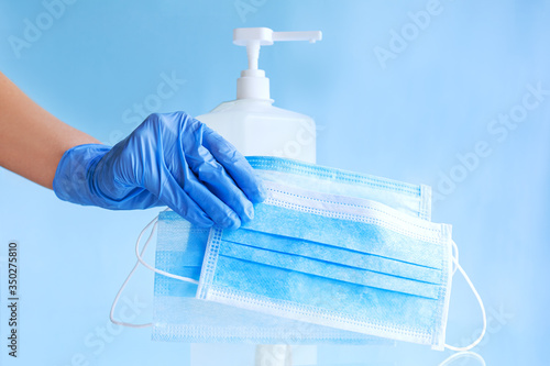 Medical face masks, surgical protective disposable face mask in doctor hand in blue gloves. Bottle alcohol sanitizer gel. Coronavirus covid 19 virus prevention hygiene on blue background.