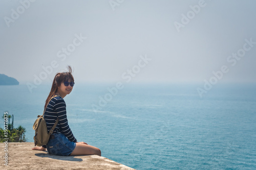 Happy traveler Asian woman sitting on a cliff that sees the sea beach at Ko Sichang, Thailand. Summer travel vacation concept.