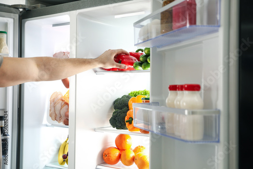 Young man taking bell pepper out of refrigerator, closeup
