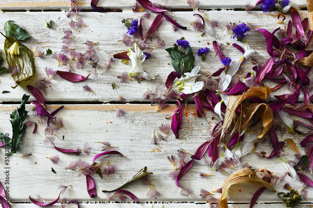 A top view image of loose dried flower petals on a white washed wooden table top. 