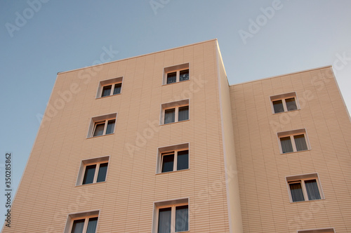 Modern new building with a lot of flats. There are windows and balconies. Light blue sky above