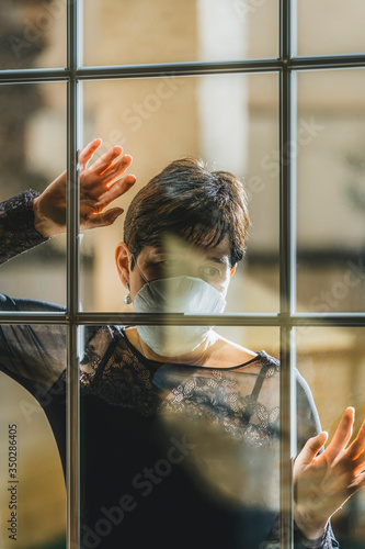 Corona virus. Woman sick with Covid wearing a protective mask and recovering at home from the disease after quarantine looking out the window at Patient Street in isolation to prevent infection. 