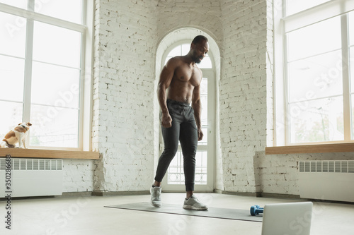 Wallpaper Mural Young african-american man training at home during quarantine of coronavirus outbreak, doinc exercises of fitness, aerobic. Staying sportive during insulation. Wellness, movement concept. Torontodigital.ca
