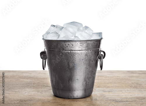 Metal bucket with ice cubes on wooden table against white background