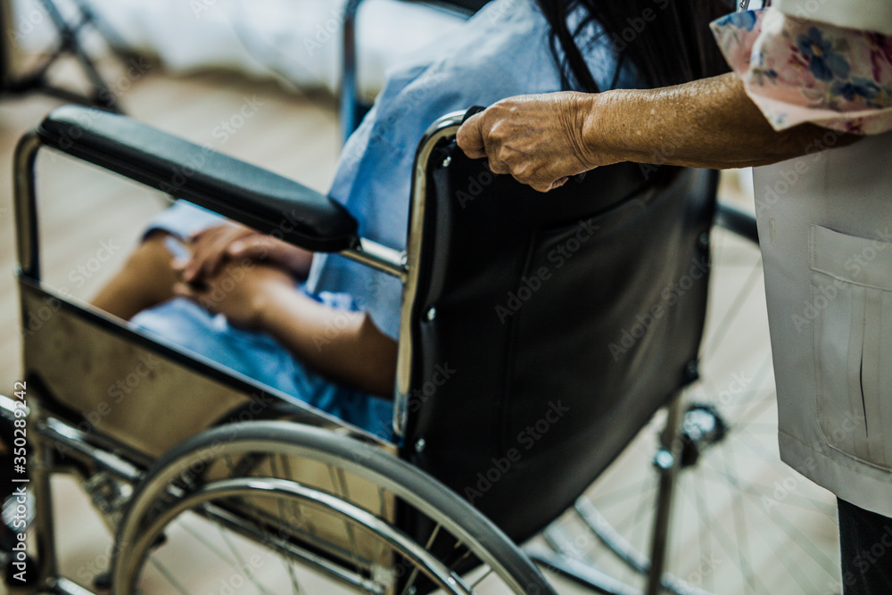 Obraz premium Doctor take care woman patient sit on the wheelchair. Hand take wheelchair to foward.