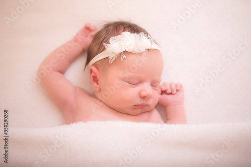 Close-up beautiful sleeping baby girl. Newborn baby girl, sleep on a blanket. A portrait of a beautiful, seven day old, newborn baby girl wearing a large, fabric rose headband. Closeup photo.