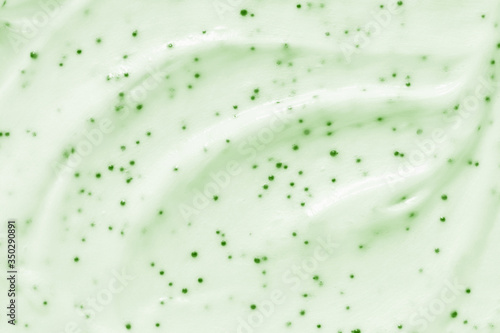 Face cream scrub texture background. Green color exfoliating skincare product smear smudge swatch. Gentle creamy scrub cleanser strokes closeup photo