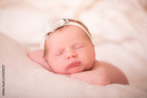 Newborn baby girl wearing a headband is sleeping on her tummy.
