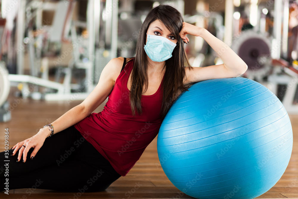 Fototapeta premium Piękne sportowe womanposing przeciwko niebieskiej piłce w masce, koncepcja koronawirusa