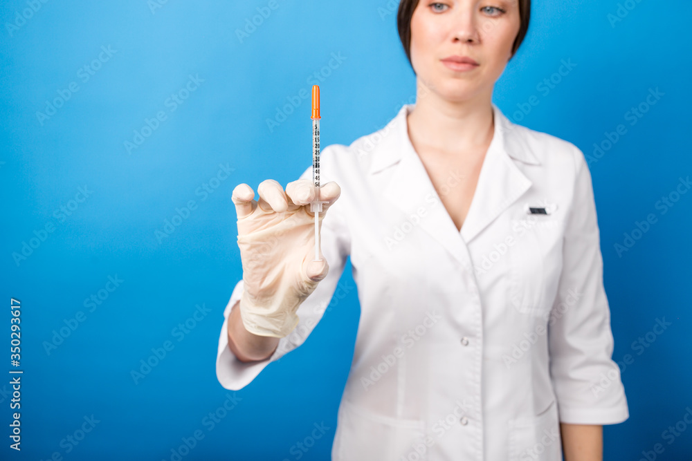 Female doctor holding a syringe with medicine in the foreground standing on a blue background Female doctor holding a syringe with medicine in the foreground standing on a blue background