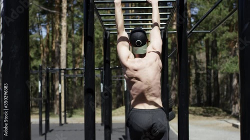 Adult caucasian athlete is exercising on swedis wall topless at the gym at the park during his daily workout, back shot photo