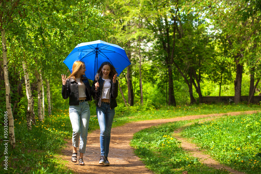 Fototapeta premium Two happy girlfriends walk in the park in rainy weather