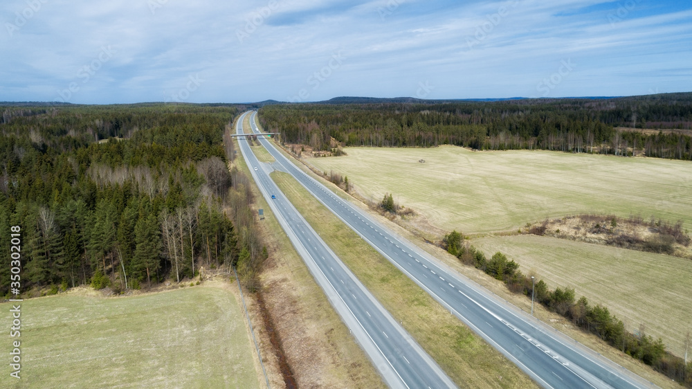 Aerial view of a highway going through the forest and fields. Highway in Finland, European union.