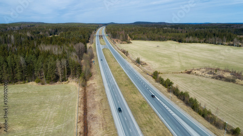 Aerial view of green spring forest with a road. Captured from above with a drone. Cars are moving on the highway surrounded by green trees.