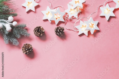 Christmas tree branch, pine cones and luminous garland on a pink background. Happy New Year greeting card and banner