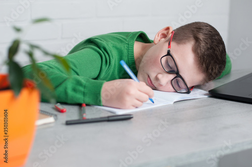 teenager tired puts his head on table, writing hometask in copybook in glasses photo