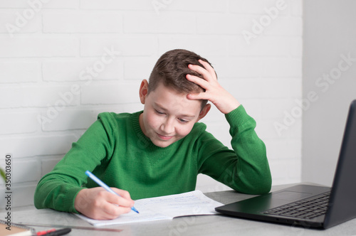 pupil boy focused on hometasks writing in copybook sitting at table in light room