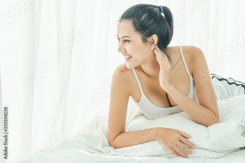 Beautiful asian woman just woke up and laying on the bed smile and looking outside. Sexy look in the morning time. Copy Space.