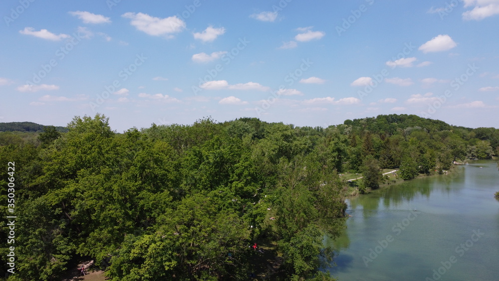 drone shot over lake with green trees and blue sky