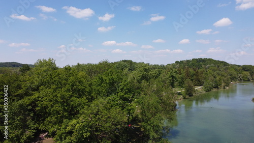 drone shot over lake with green trees and blue sky