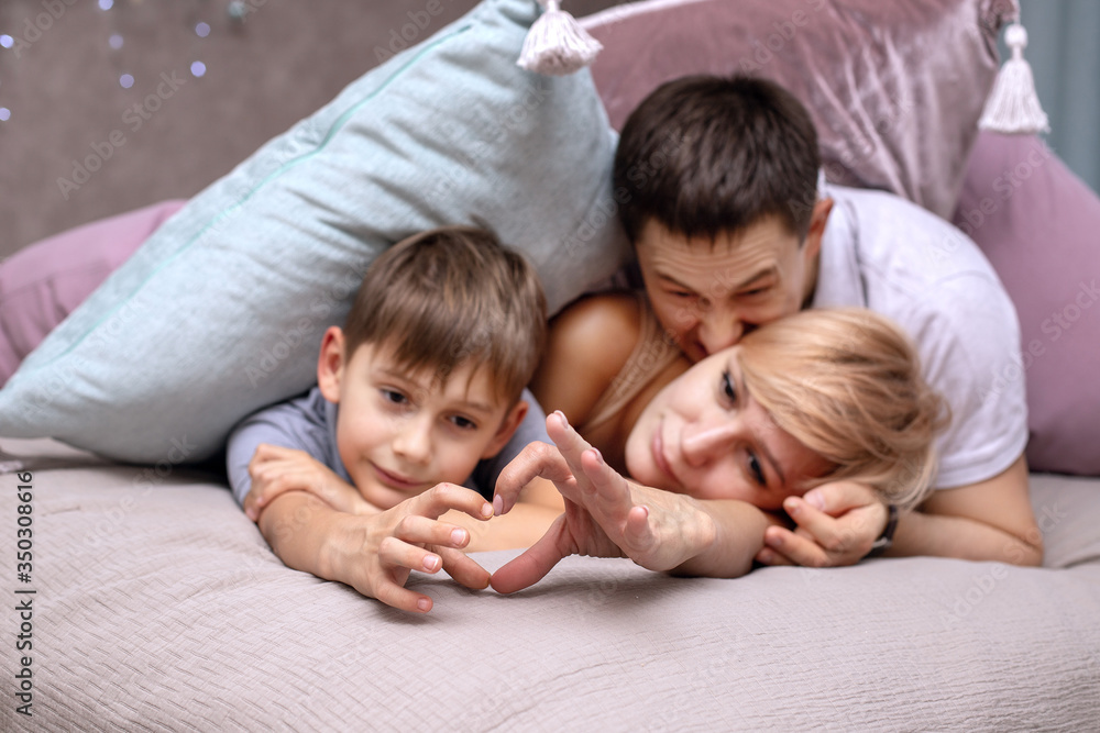 Happy family on a bed with soft pillows at home. Hands represent the heart Happy family on a bed with soft pillows at home. Hands represent the heart