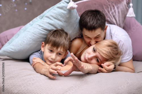 Happy family on a bed with soft pillows at home. Hands represent the heart