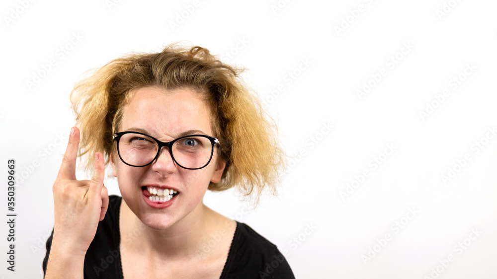 A girl rocker with yellow hair and glasses squinting one eye shows a hand gesture Heavy Metal HM on a white background. Concept of informal youth and heavy rock.Banner A girl rocker with yellow hair and glasses squinting one eye shows a hand gesture Heavy Metal HM on a white background. Concept of informal youth and heavy rock.Banner