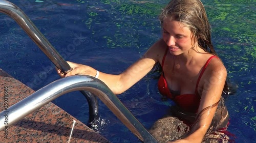 Summer season for girl climbing out of that swimming pool holding onto rails of ladder. Slow motion of turquoise water in end.
