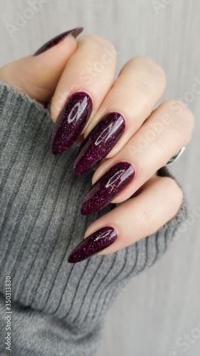 Photo Female hand with long nails and a dark red burgundy manicure holds a bottle of n
